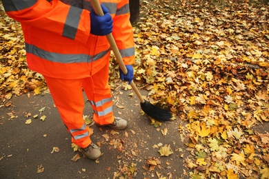 Photo of Street cleaner sweeping fallen leaves outdoors on autumn day