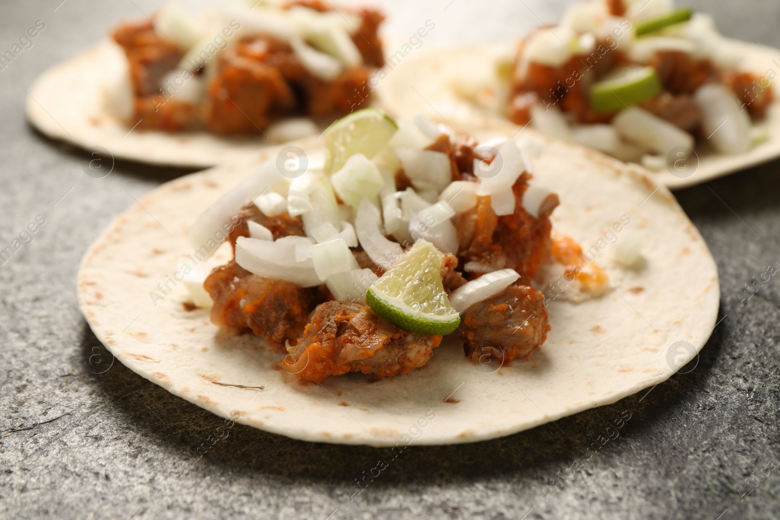 Photo of Delicious tacos with vegetables, meat and lime on grey textured table, closeup