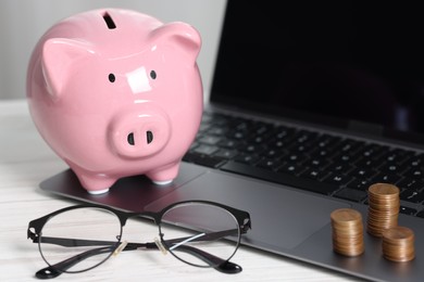 Photo of Piggy bank, glasses, coins and laptop on white table