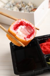 Photo of Holding delicious sushi roll with chopsticks over soy sauce on table, closeup