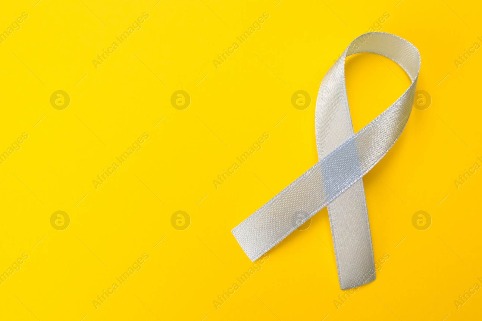 Photo of International Psoriasis Day. Ribbon as symbol of support on yellow background, top view. Space for text