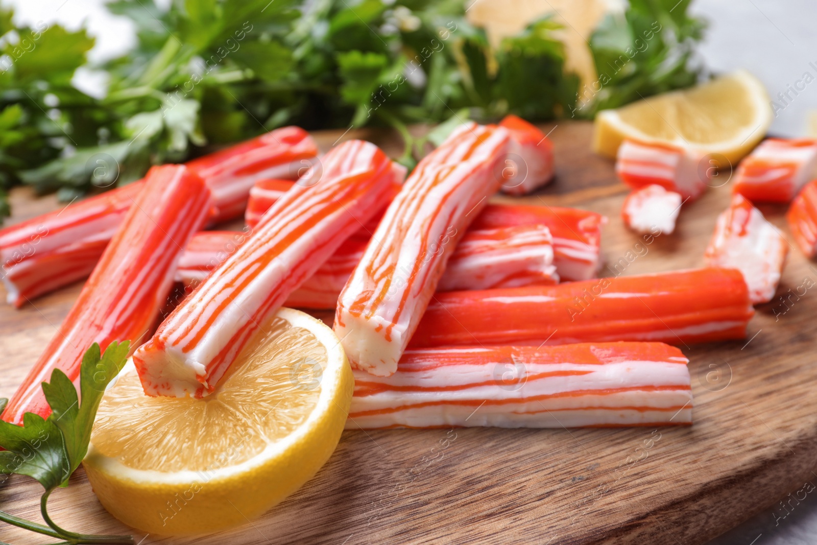 Photo of Delicious crab sticks with lemon and parsley on wooden board, closeup