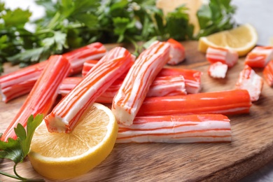 Photo of Delicious crab sticks with lemon and parsley on wooden board, closeup