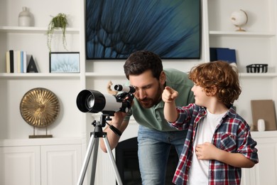 Photo of Little boy with his father looking at stars through telescope in room