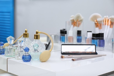 Photo of Different makeup products and bottles of perfumes on white dressing table