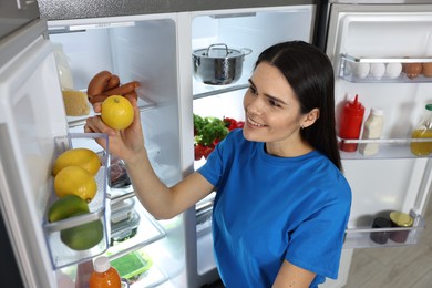 Photo of Young woman taking lemon out of refrigerator indoors