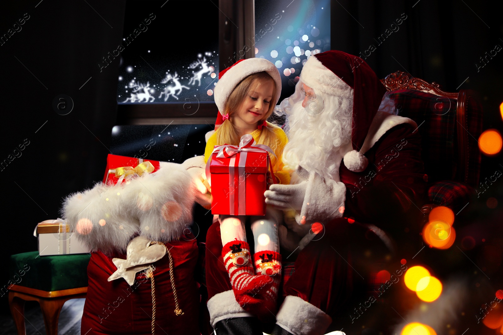 Image of Santa Claus with little girl in armchair at home. Christmas time