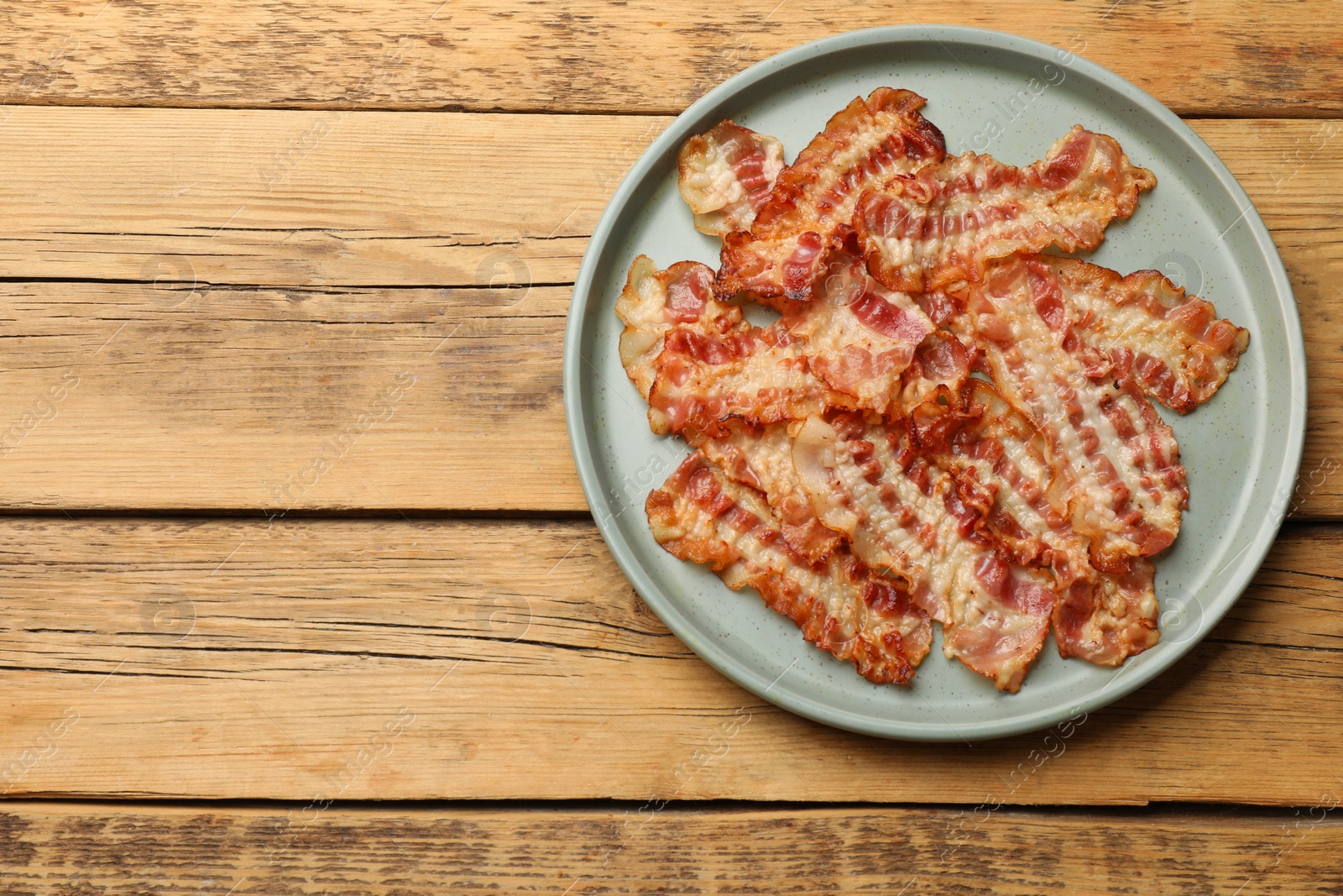 Photo of Delicious fried bacon slices on wooden table, top view. Space for text