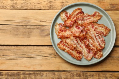 Photo of Delicious fried bacon slices on wooden table, top view. Space for text