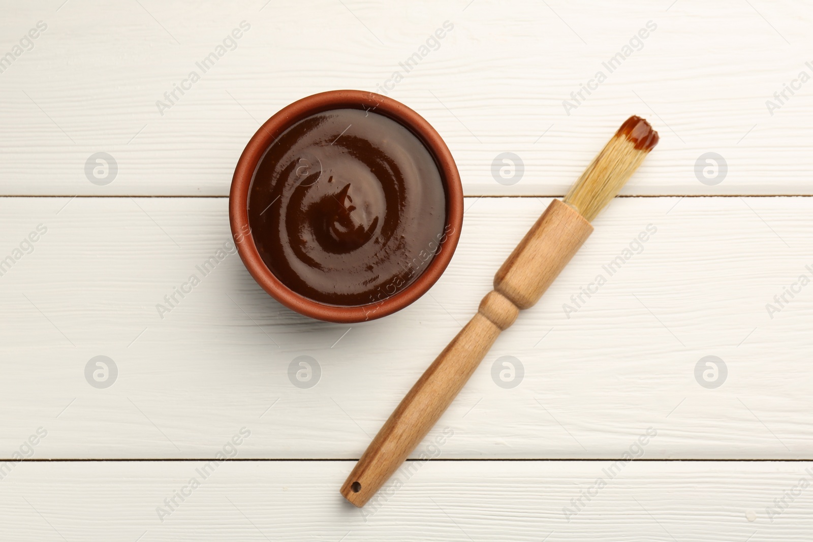 Photo of Tasty barbeque sauce in bowl and brush on white wooden table, top view