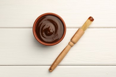 Photo of Tasty barbeque sauce in bowl and brush on white wooden table, top view