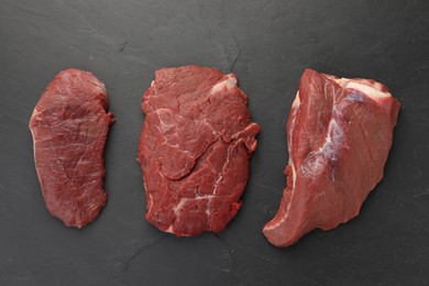 Pieces of raw beef meat on black table, flat lay