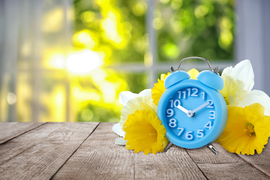 Image of Alarm clock and flowers on table against blurred background, space for text. Spring time