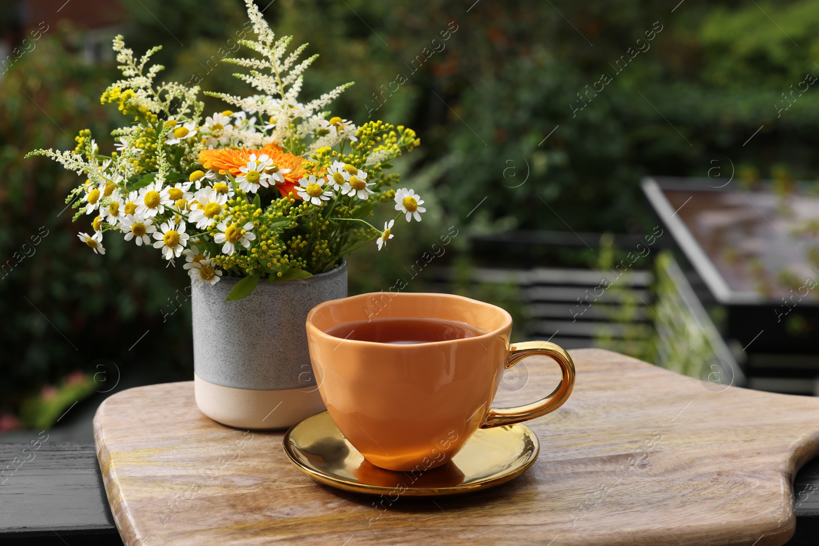 Photo of Cup of delicious chamomile tea and fresh flowers outdoors. Space for text