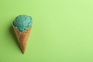 Photo of Delicious spirulina ice cream in waffle cone on color background, top view. Space for text