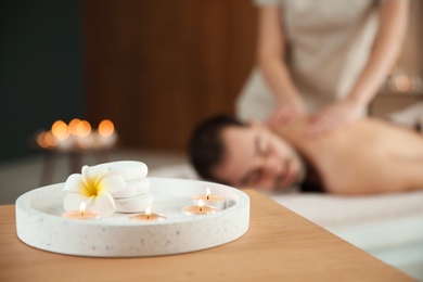 Composition with candles and blurred man receiving massage in spa salon. Space for text