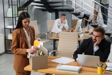 Young dismissed woman packing stuff into box at office