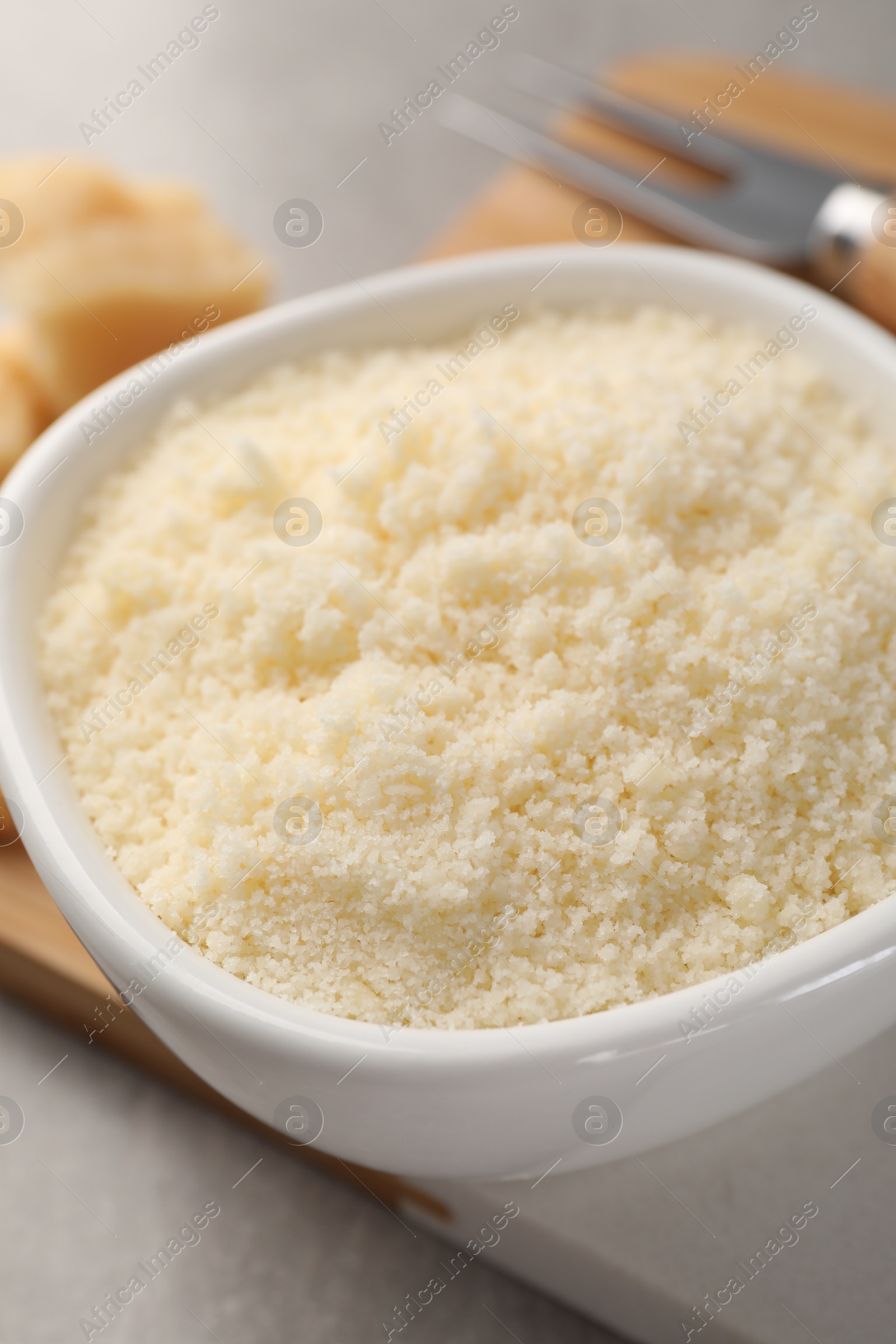 Photo of Bowl with grated parmesan cheese on light table, closeup