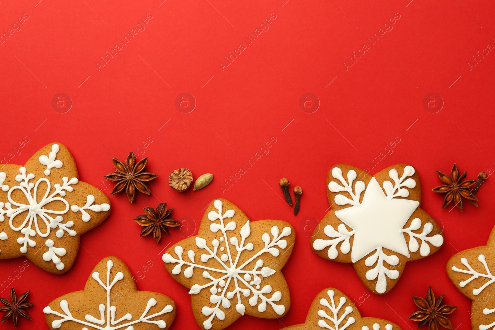 Photo of Tasty star shaped Christmas cookies with icing and spices on red background, flat lay. Space for text