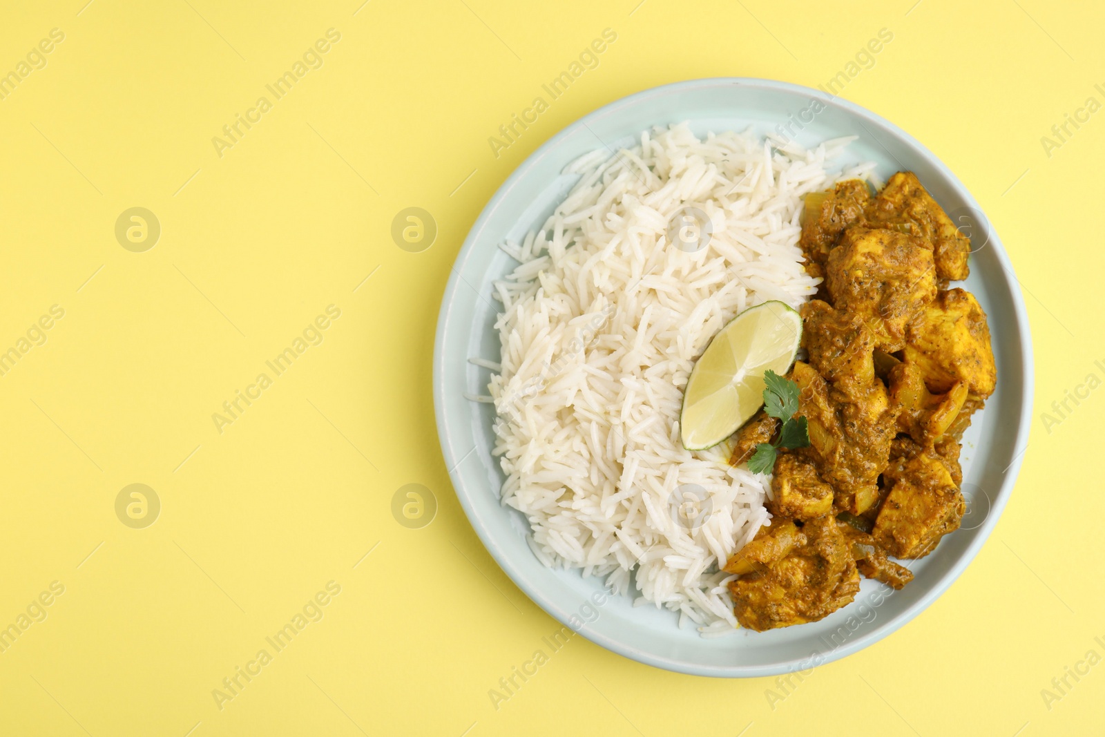 Photo of Delicious chicken curry with rice on yellow background, top view. Space for text