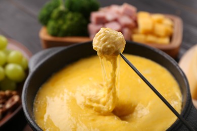 Dipping piece of ham into fondue pot with melted cheese on table, closeup