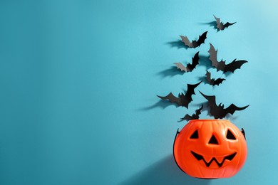 Photo of Flat lay composition with paper bats and plastic pumpkin basket on light blue background, space for text. Halloween decor