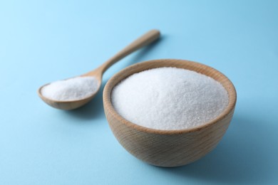 Photo of Organic white salt in bowl and spoon on light blue background