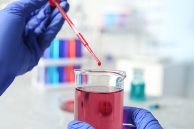 Scientist dripping reagent into beaker with sample in chemistry laboratory, closeup