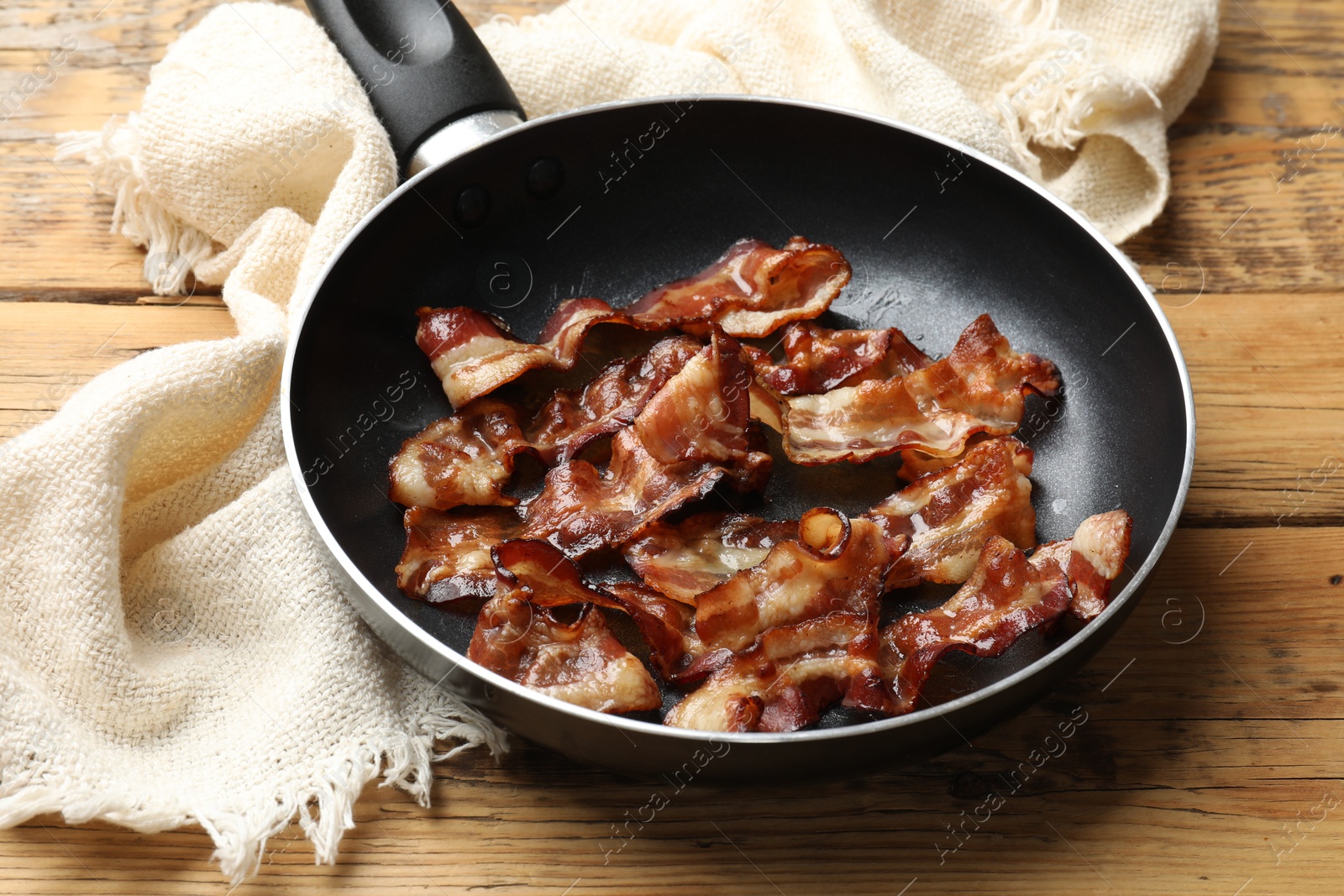 Photo of Delicious bacon slices in frying pan on wooden table