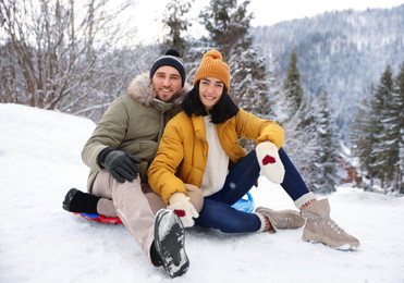 Happy couple sliding on snowy hill. Winter vacation