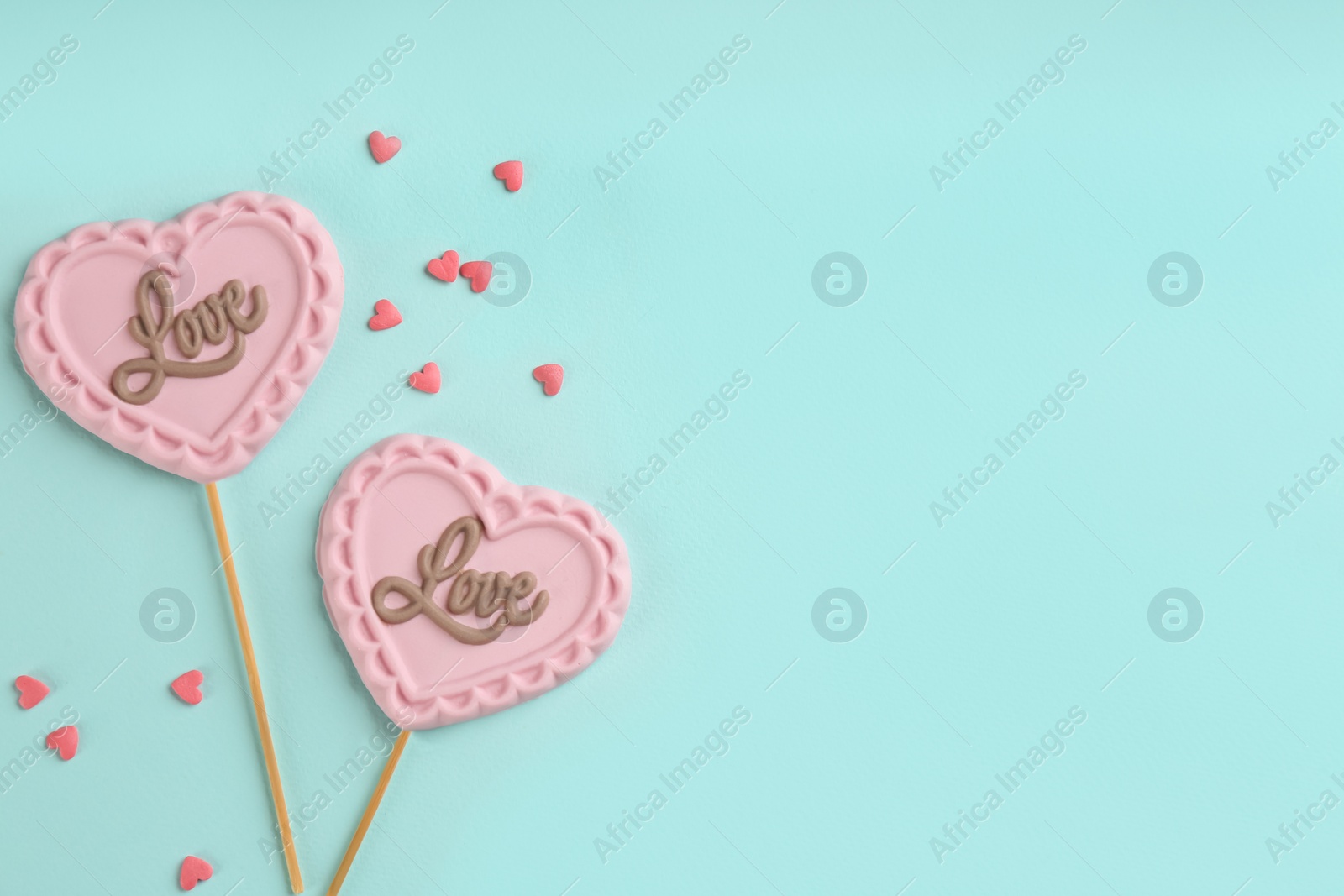 Photo of Chocolate heart shaped lollipops and sprinkles on turquoise background, flat lay. Space for text