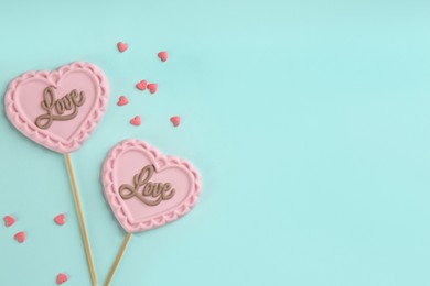 Chocolate heart shaped lollipops and sprinkles on turquoise background, flat lay. Space for text