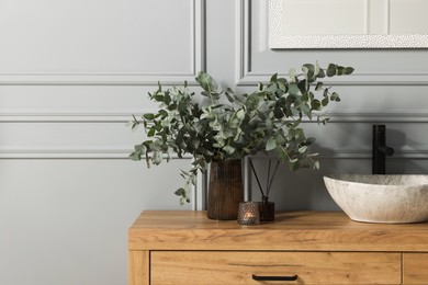 Photo of Eucalyptus branches, candle and aroma sticks near vessel sink on bathroom vanity. Interior design