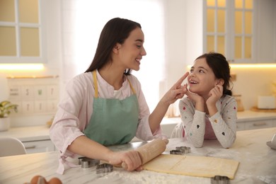 Mother with her cute little daughter having fun while rolling dough in kitchen