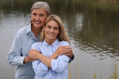 Photo of Happy mature mother and her daughter hugging near pond, space for text