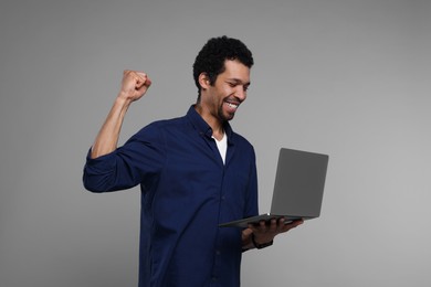 Emotional man with laptop on grey background