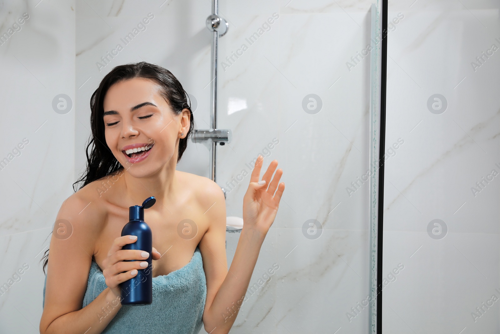 Photo of Young woman with bottle of gel singing while taking shower. Space for text