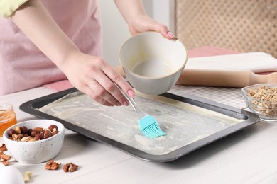 Photo of Making delicious baklava. Woman buttering dough in baking pan at white wooden table, closeup