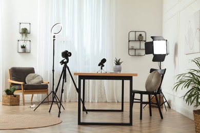 Photo of Camera and lighting equipment on tripods near table in room. Blogger workplace