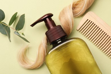 Photo of Lock of hair, shampoo bottle and wooden comb on olive background, flat lay