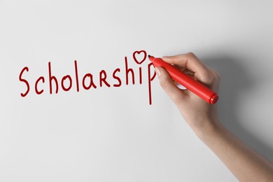 Woman writing word SCHOLARSHIP on white paper, closeup