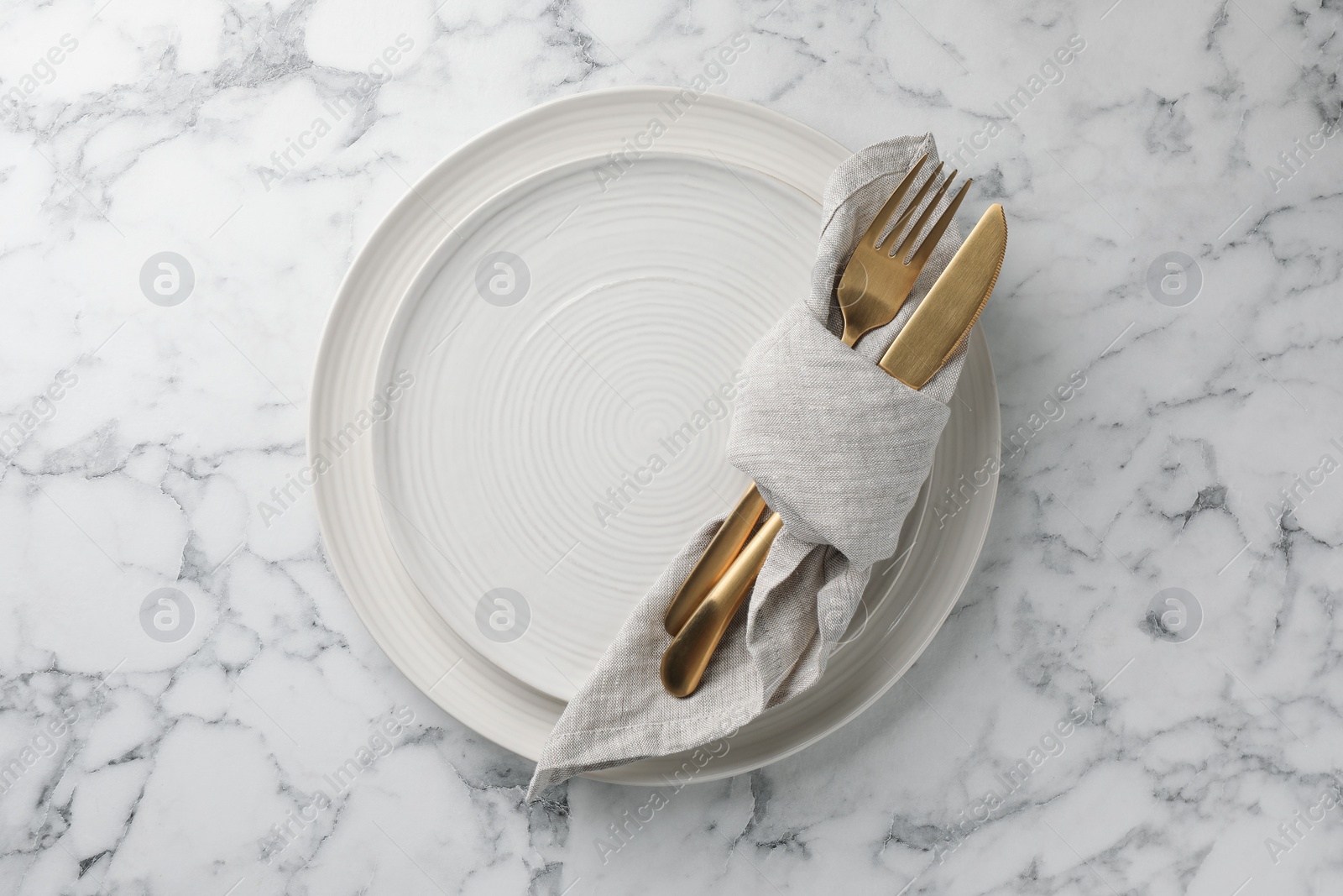 Photo of Stylish setting with cutlery, napkin and plates on white marble table, top view