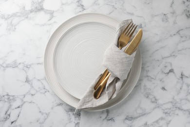 Stylish setting with cutlery, napkin and plates on white marble table, top view