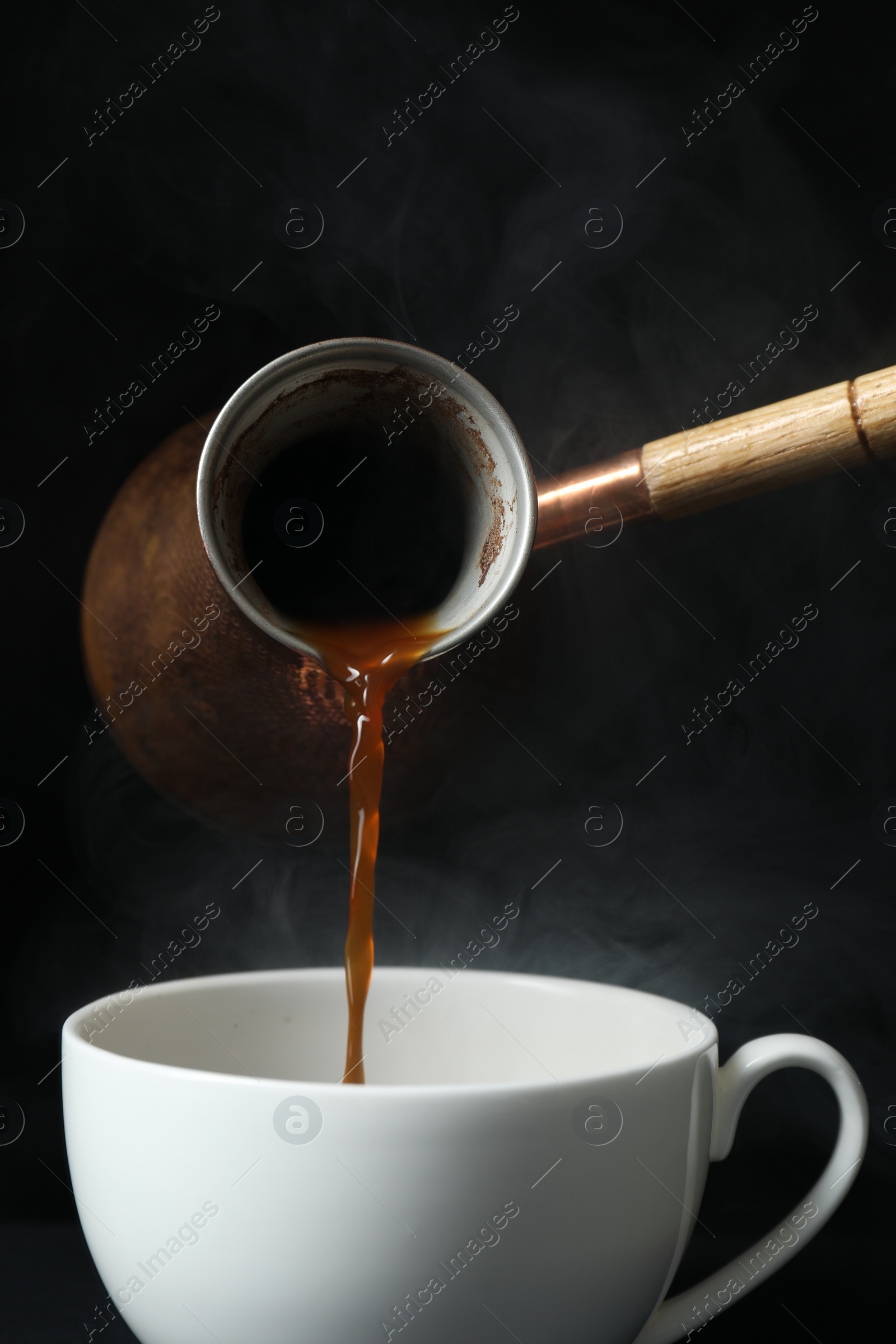 Photo of Turkish coffee. Pouring brewed beverage from cezve into cup against black background