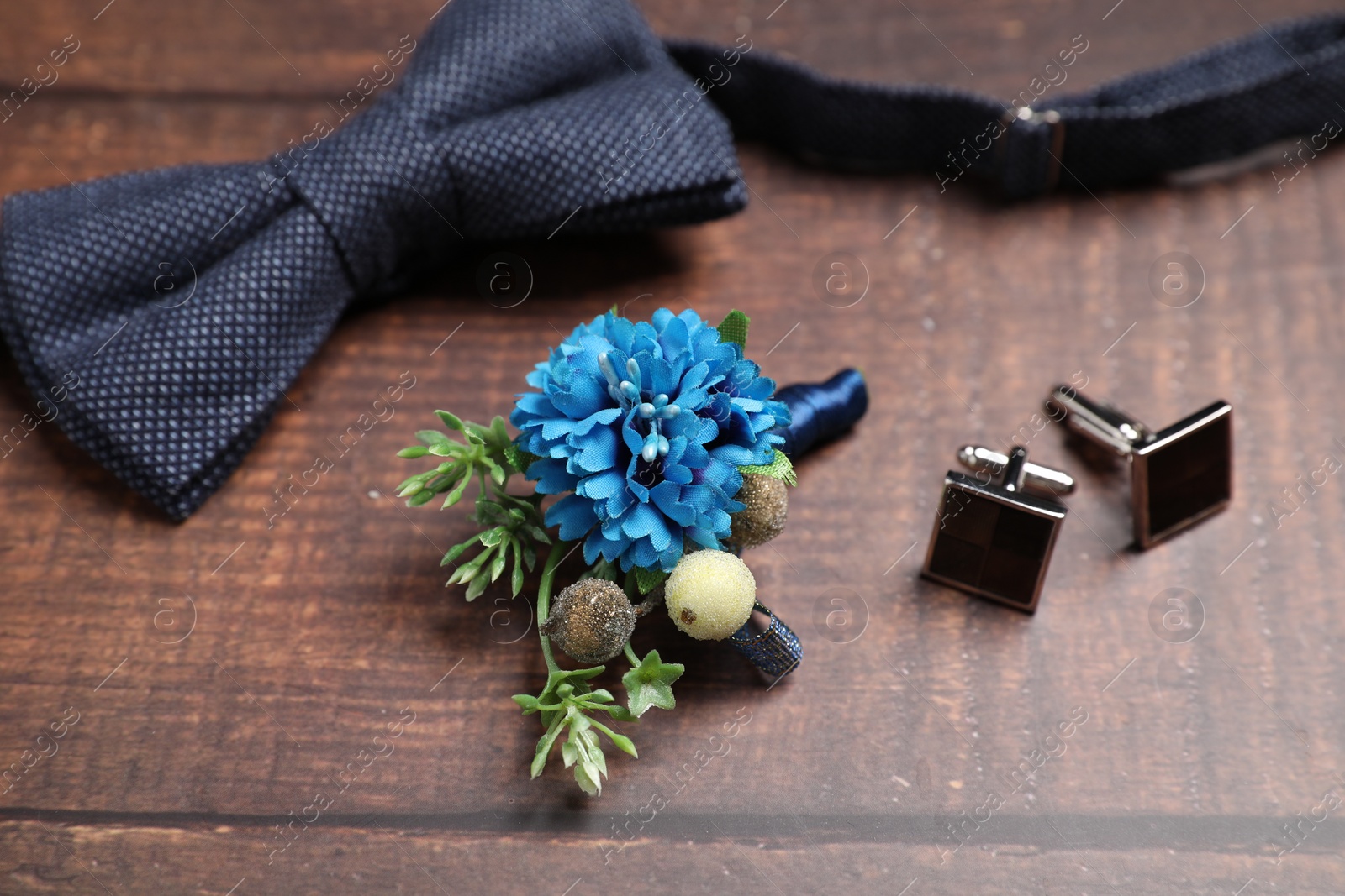Photo of Wedding stuff. Stylish boutonniere, bow tie and cufflinks on wooden background, closeup