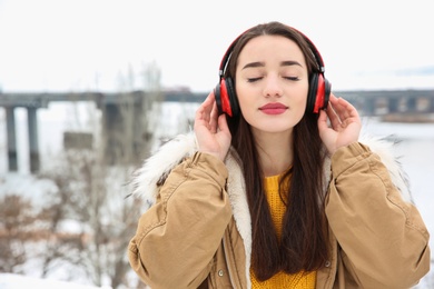 Photo of Beautiful young woman listening to music with headphones outdoors. Space for text