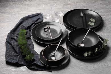 Photo of Stylish table setting. Dishes, cutlery, glasses and eucalyptus branches on grey surface