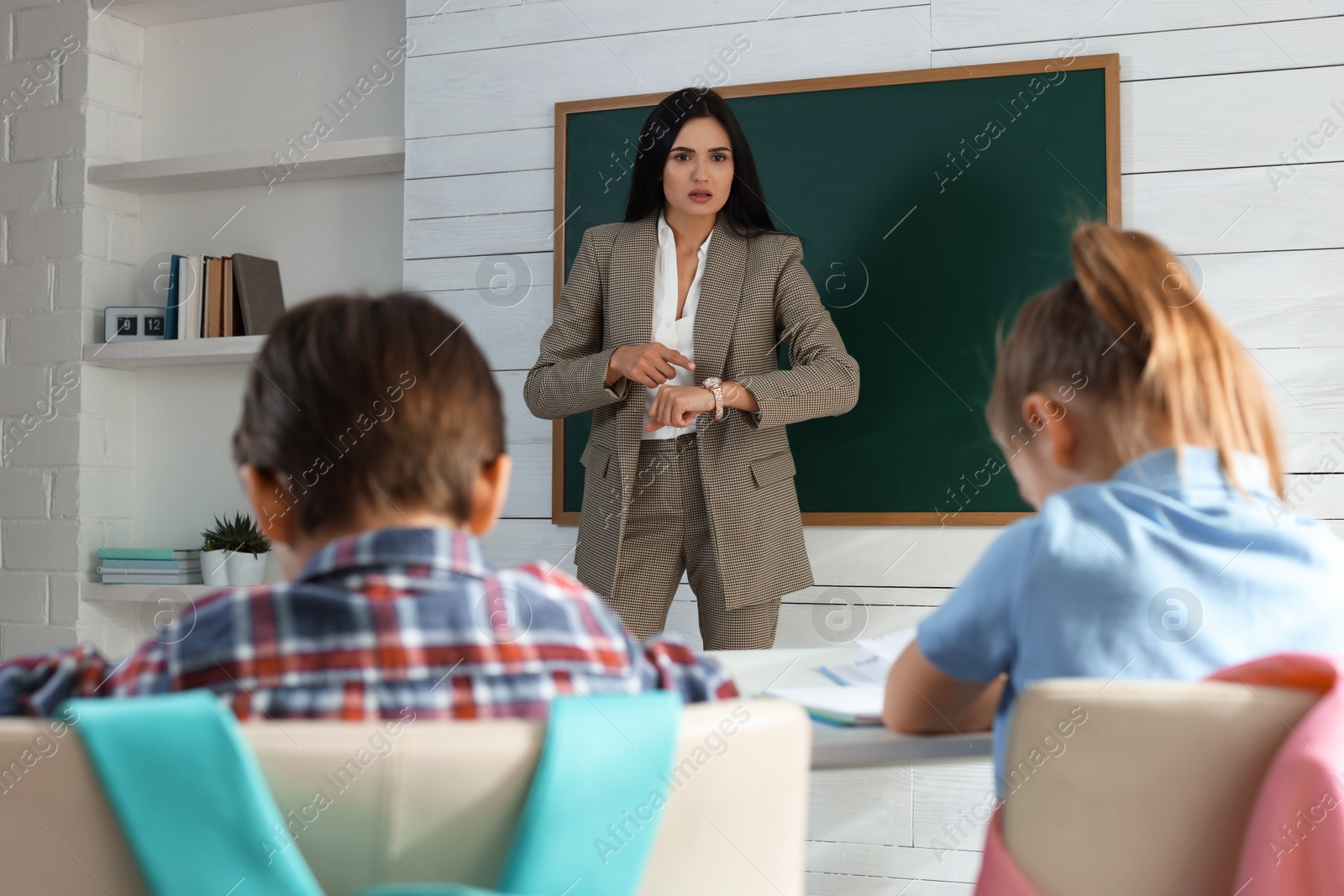 Photo of Teacher pointing on wrist watch while scolding pupils for being late in classroom