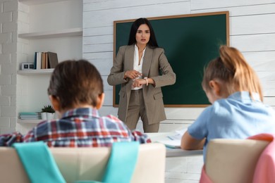 Teacher pointing on wrist watch while scolding pupils for being late in classroom