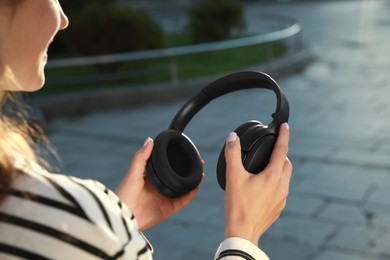 Photo of Woman holding black headphones on city street, closeup